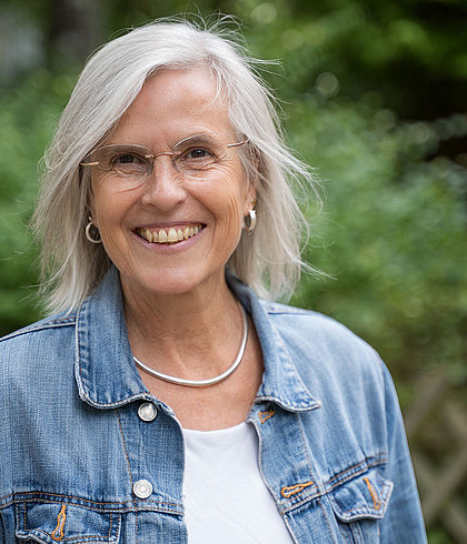 Lächelnde Frau mit grauen Haaren, Brille und Jeansjacke